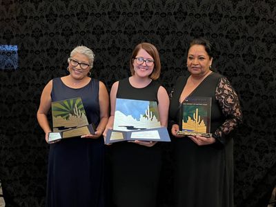 Three individuals stand posing for a photo while holding awards.