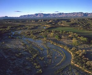 Ariel shot of a river and a green landscape with mountains in the distance.