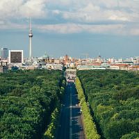 Aerial view of the city of Berlin, with a road dividing a forest leading to the buildings in the city.