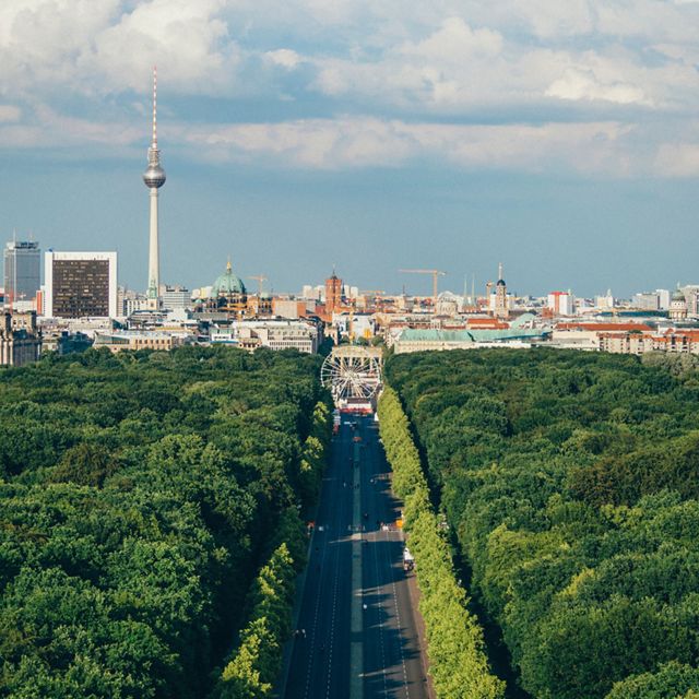 A lush forest straddles a broad boulevard that leads into central Berlin in the distance.