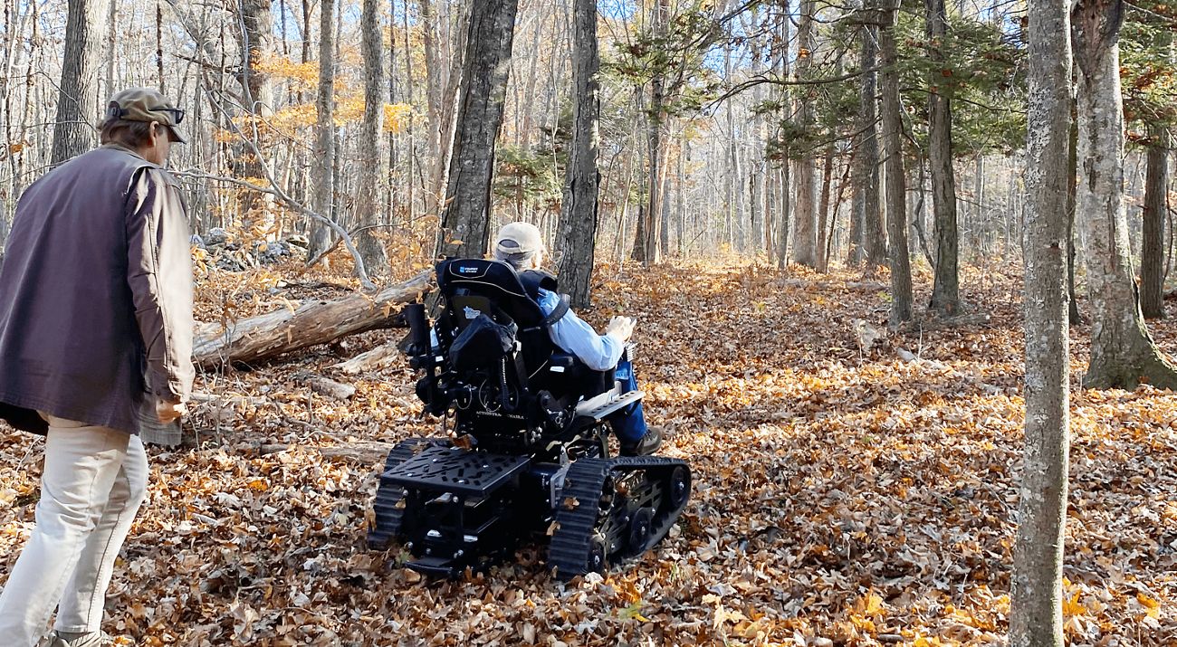 A person rides an all-terrain wheel trail through a leafy trail in a wooded landscape.