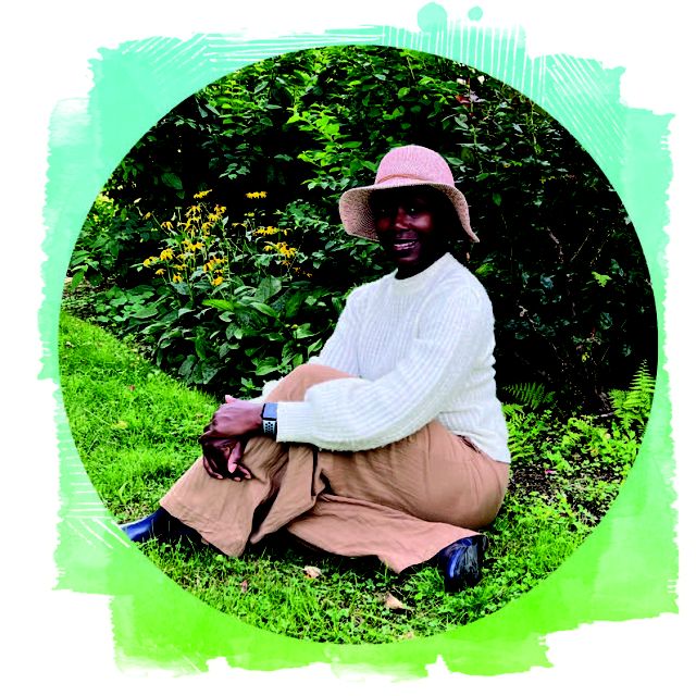A woman in a floppy hat sits on the grass.