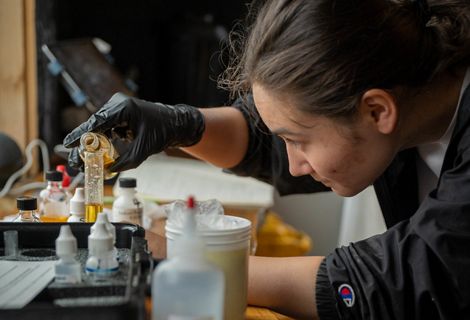 A scientist watches carefully while pouring a liquid from a beaker into a test tube.