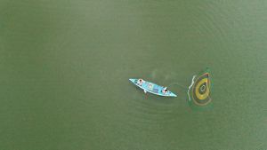 An aerial view of two people on a blue boat, using a net to harvest shrimp.