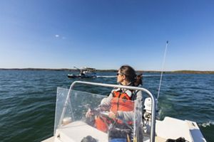 A woman in an orange life vest piloting a boat on water.