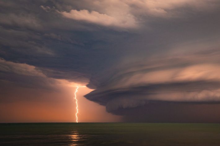 A lightning strike in the distance against a peach coloured storm clouds