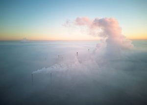 An aerial shot of smoke stacks from a factory spewing smoke.