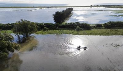 Two girls riding horses on heavily flooded paddocks.