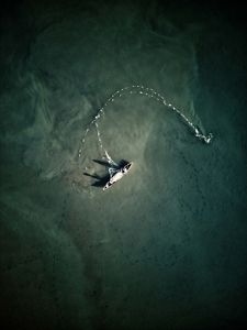 An aerial view of a fishing boat trying to cast nets in muddy waters.