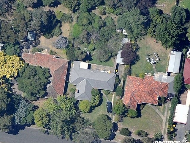An aerial view of 3 houses surrounded by tree canopy