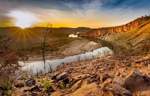 Sunset over a river with a rocky bank and hills.