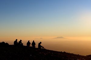 A group of people sitting on a peak at sunrise.