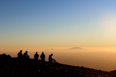 A group of people sitting on a peak at sunrise.