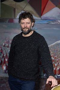 A man in a black jumper standing in front of a painting.