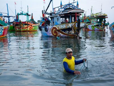 a man up to his waist in water near some fishing boats.