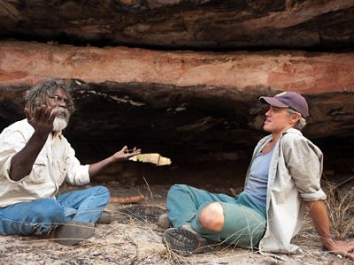 two men sitting outside on the ground talking.