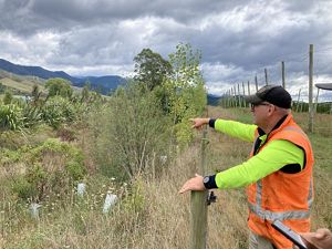 A man points at plants and bushes on farmland.