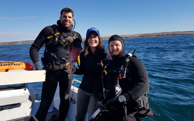 Three people in scuba gear smiling at the camera in a boat.