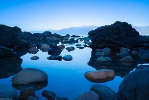 A small water pool surrounded by rocks on top of a mountain at dusk.