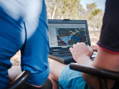 two people looking at a laptop with a GIS map on the screen.