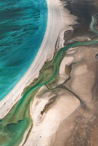 An aerial of the various colours of ocean water meeting the sand on the beach.