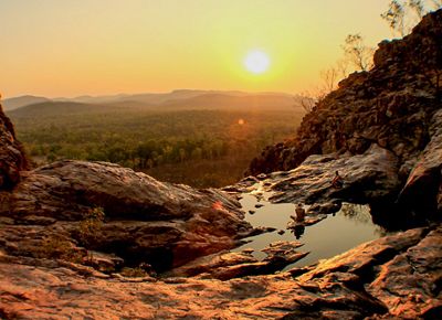 Two people sitting on the edge of a rock pool overlooking bushland at sunset