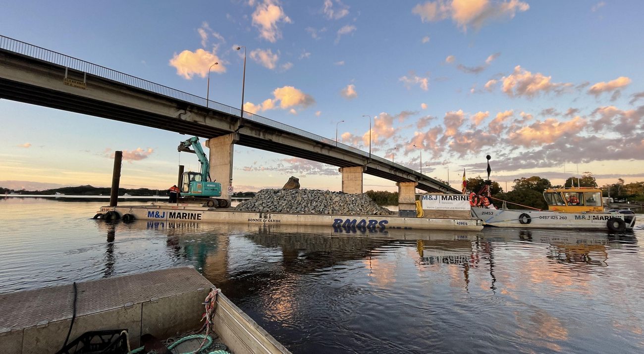 A barge with rocks and construction equipment going under a bridge