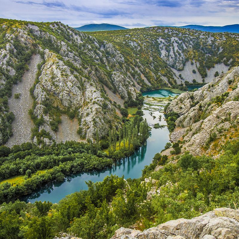 A canyon of the Krupa River that meanders through trees, plants and rocks.