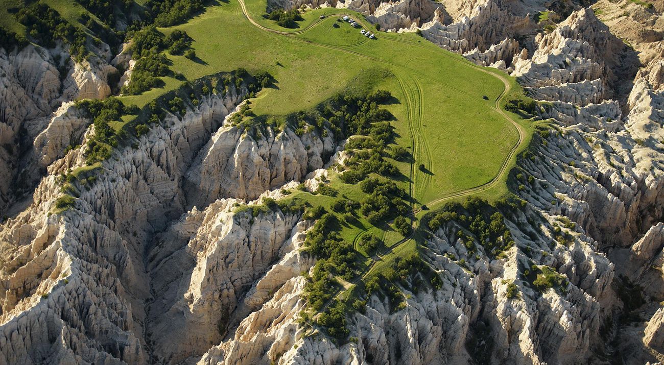 Photo of Badlands National Park, with green-topped hills and steep, eroded sides descending into narrow canyons.