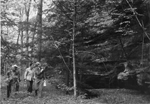 A black and white photo of three people walking through a forest. 