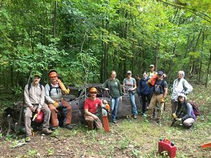 Volunteer crew posing with tools with forest background.