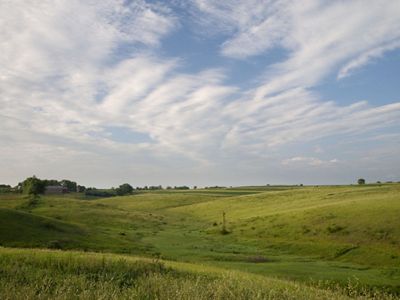 Green rolling prairie fields under a partially cloudy blue sky.