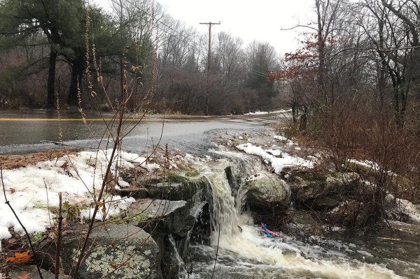 Water rushing across a road and over the rocks along the side of a road instead of going through the culvert.