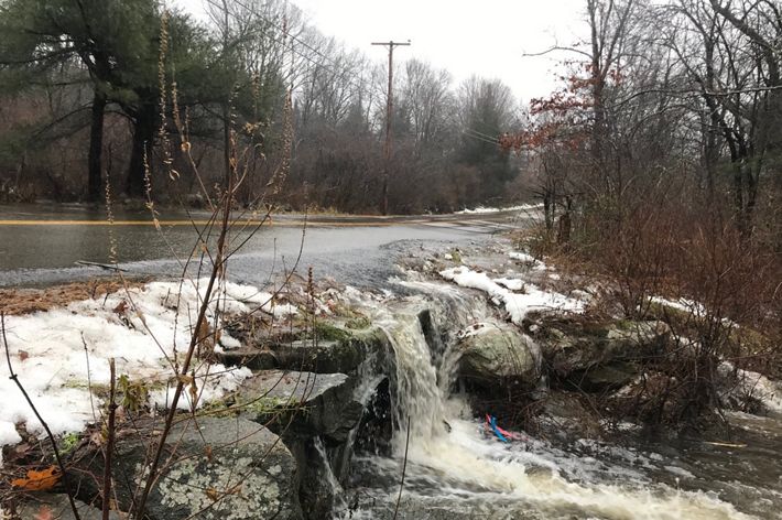 Water rushing across a road and over the rocks along the side of a road instead of going through the culvert.