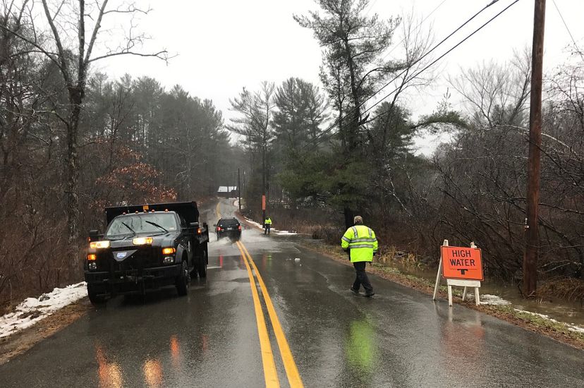 A wet road with a utility truck and a worker in a reflective vest.