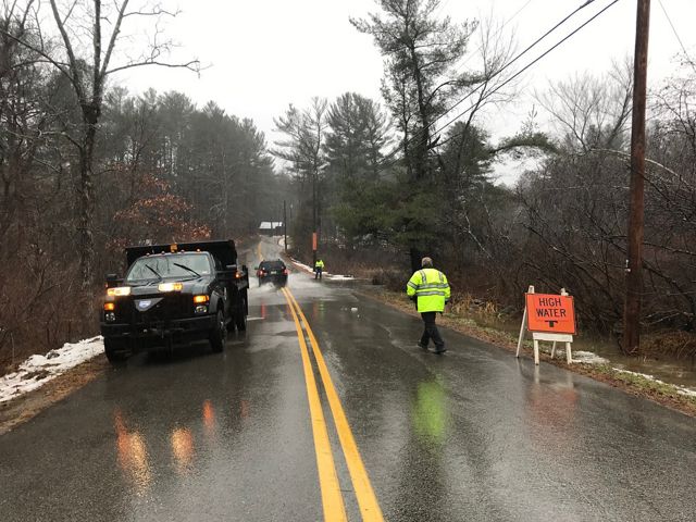 A wet road with a utility truck and a worker in a reflective vest.