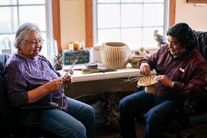 A woman and a man sit together weaving intricate baskets.