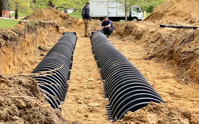 A shallow ditch with two, long parallel black plastic conduits in it.