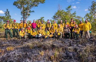 A large group of people pose together for a photo at the conclusion of a controlled burn.