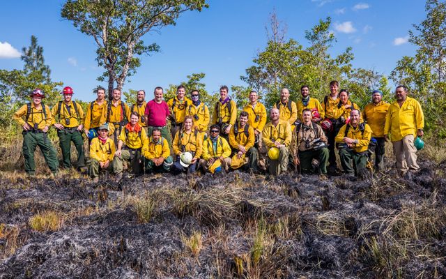 A large group of people pose together for a photo at the conclusion of a controlled burn. 