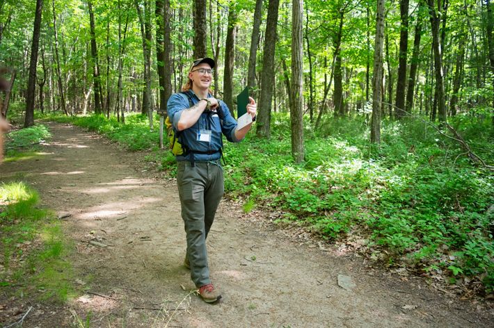 A man in a hat walks through a forest along a dirt trail.