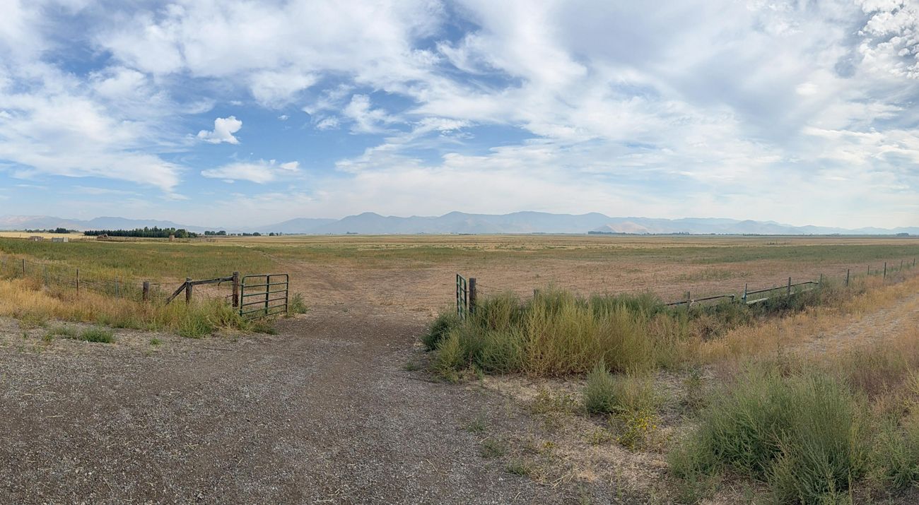 Panoramic view with open metal gate centered, opening into empty field.