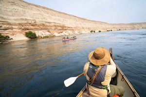 A rear view image features a person canoeing on a wide river.
