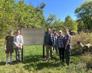 Volunteers stand next to Big Walnut Nature Preserve wood-routed sign.