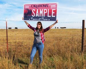 A woman excitedly holds a TNC bison license plate above her head.
