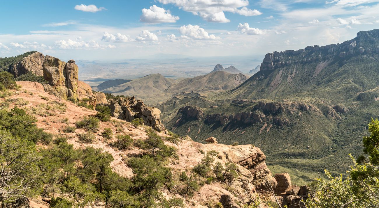 Towering rocky mountains dotted with desert shrubs and green trees.