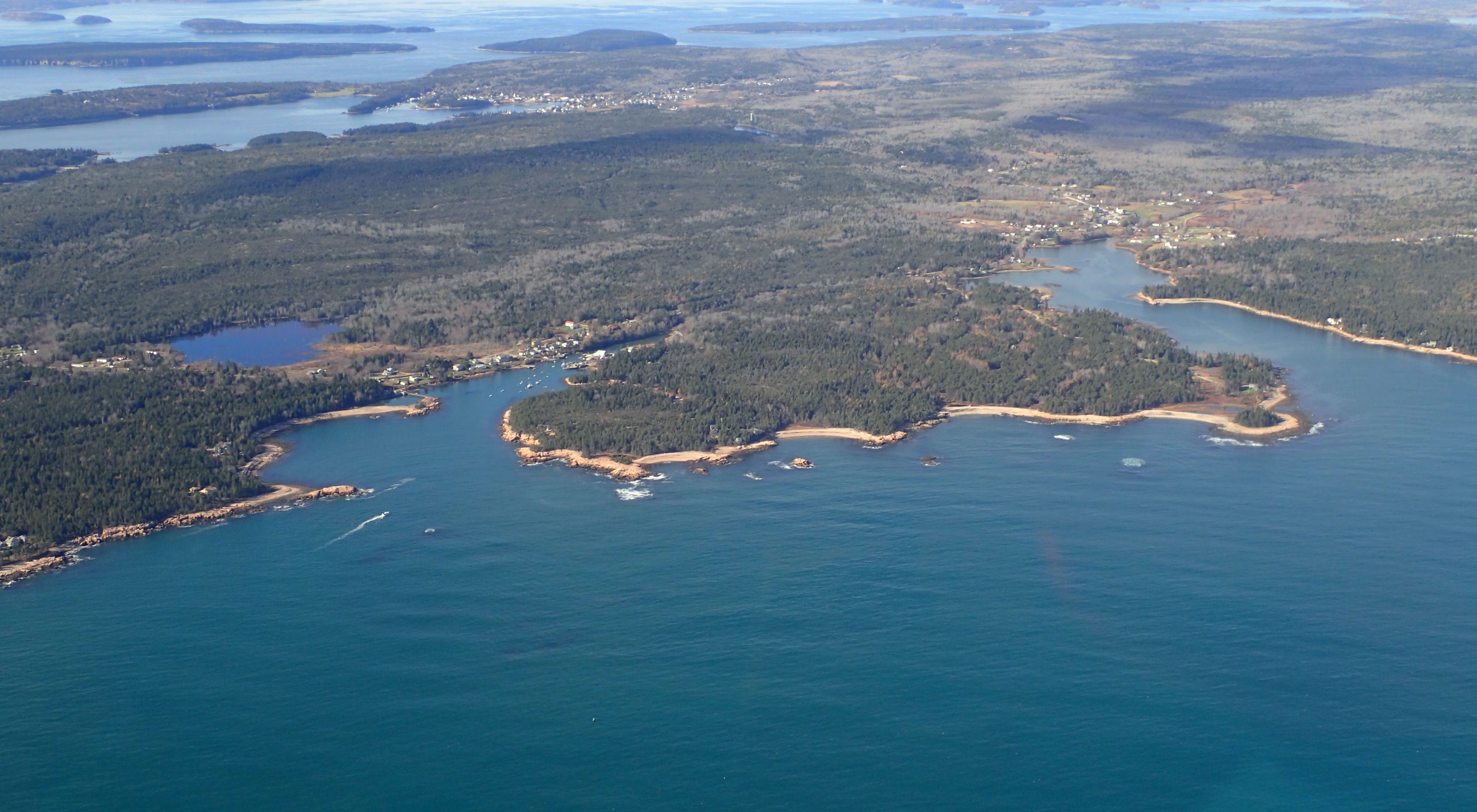 Aerial view of vast blue water framed by coastline including forest lands, islands, and small towns near the water.