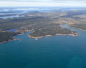 Aerial view of vast blue water framed by coastline including forest lands, islands, and small towns near the water.