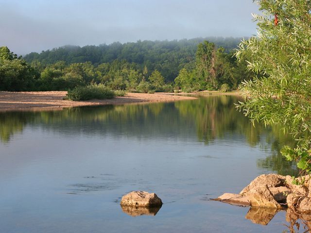 A calm river running through a forested landscape with a rocky sand bar in the distance.