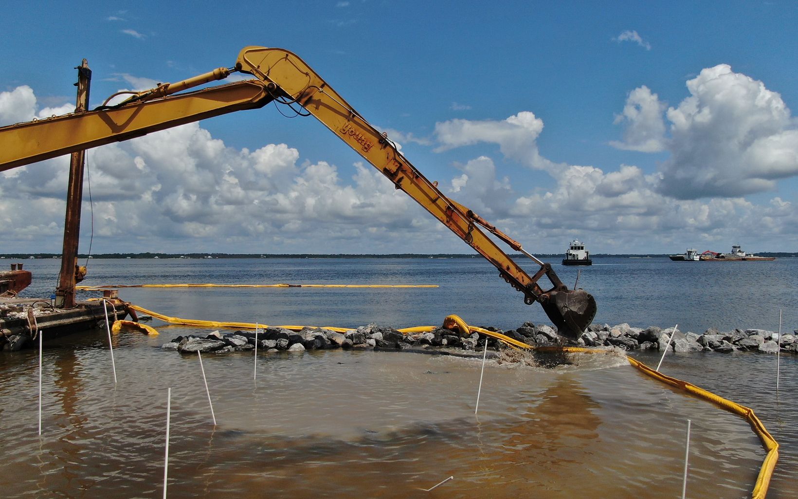 An excavator in the water works to complete reefs off-shore.